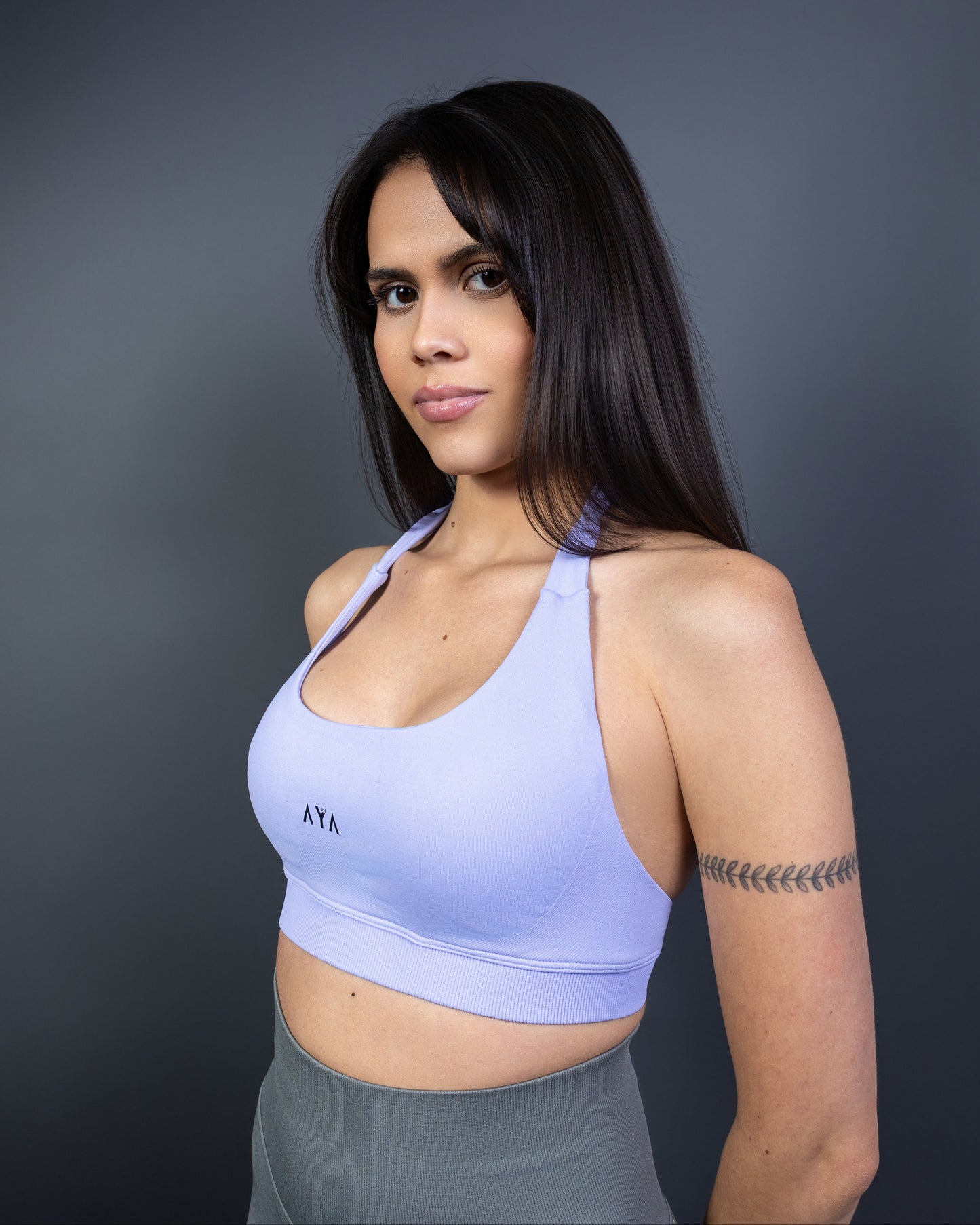 Side view of woman wearing lilac AYA halter sports bra and grey seamless leggings – soft pastel activewear that blends elegance, comfort, and modern femininity.