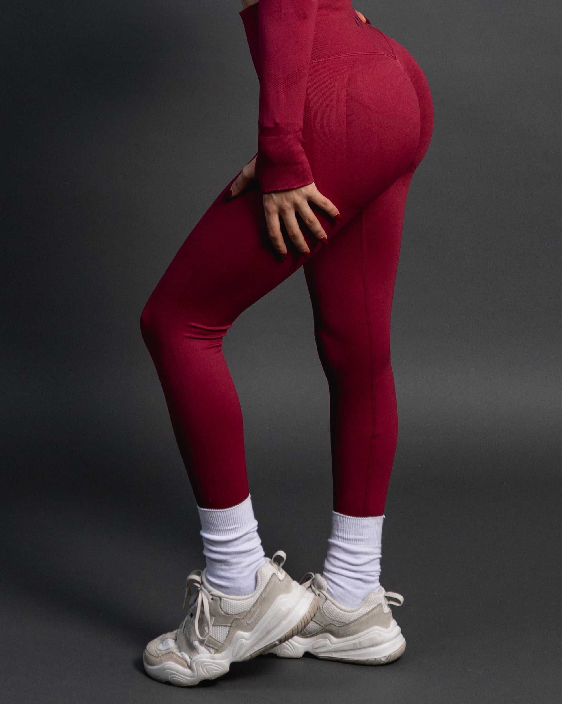 Woman wearing red high-waisted seamless AYA leggings and black sports bra – sleek, body-hugging fit designed to enhance natural curves and exude quiet confidence.