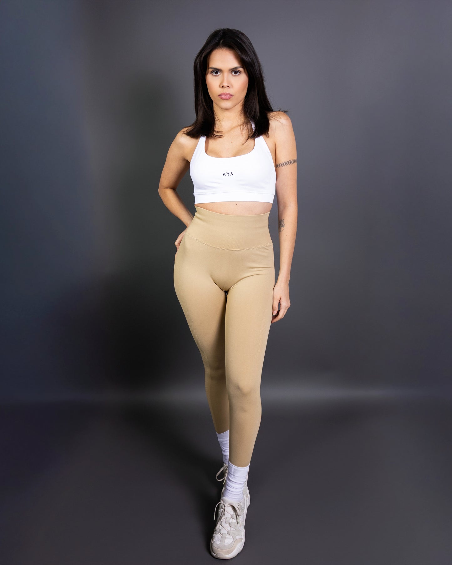 Woman wearing beige high-waisted seamless AYA leggings and white sports bra – soft, contouring activewear set designed for a sleek, confident look during workouts.