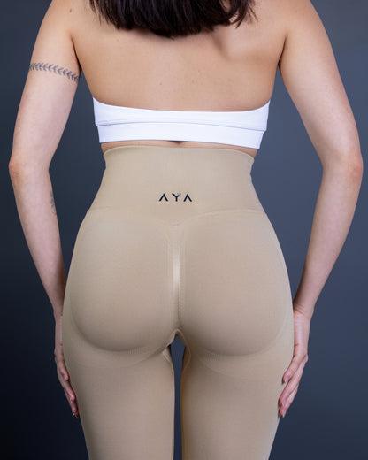 Woman wearing beige high-waisted seamless AYA leggings and white sports bra – soft, contouring activewear set designed for a sleek, confident look during workouts.