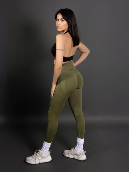 Woman wearing olive green high-waisted seamless AYA leggings and black sports bra – sleek, body-hugging fit designed to enhance natural curves and exude quiet confidence.