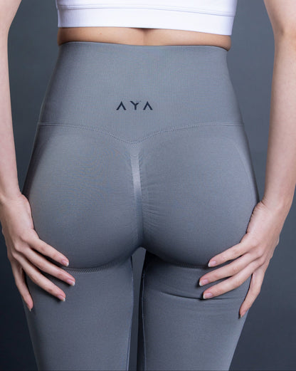 Woman wearing light grey high-waisted seamless AYA leggings and white sports bra – minimalist, sculpting activewear highlighting a sleek and confident silhouette.