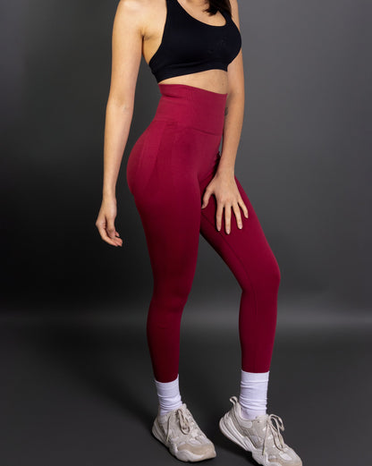 Woman wearing deep red high-waisted seamless AYA leggings and black sports bra – bold, sculpting activewear that enhances curves and radiates confidence.