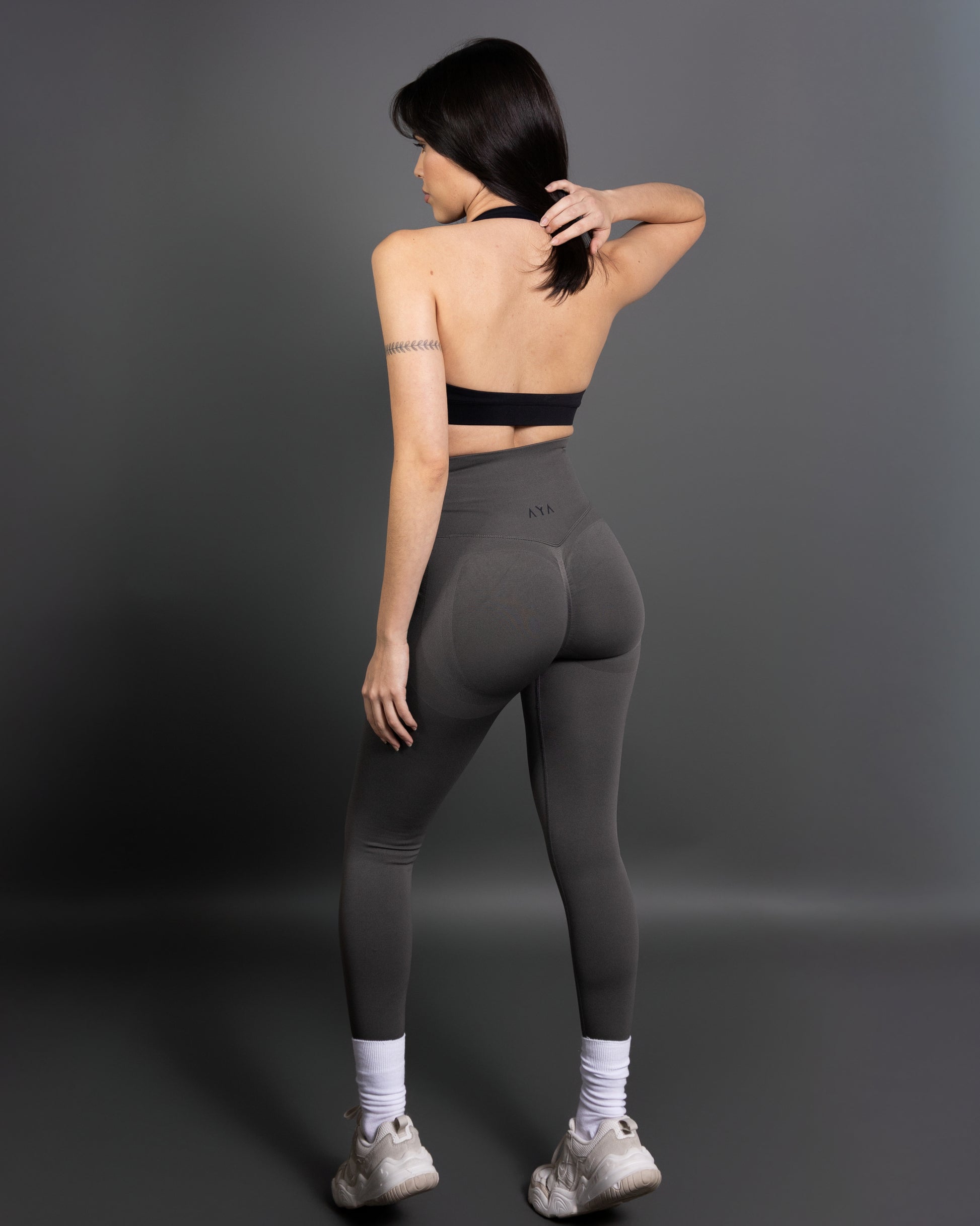 Woman wearing charcoal grey high-waisted seamless leggings and black sports bra – minimalist, body-contouring activewear for training and everyday movement.