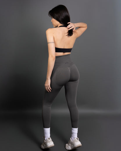 Woman wearing charcoal grey high-waisted seamless leggings and black sports bra – minimalist, body-contouring activewear for training and everyday movement.