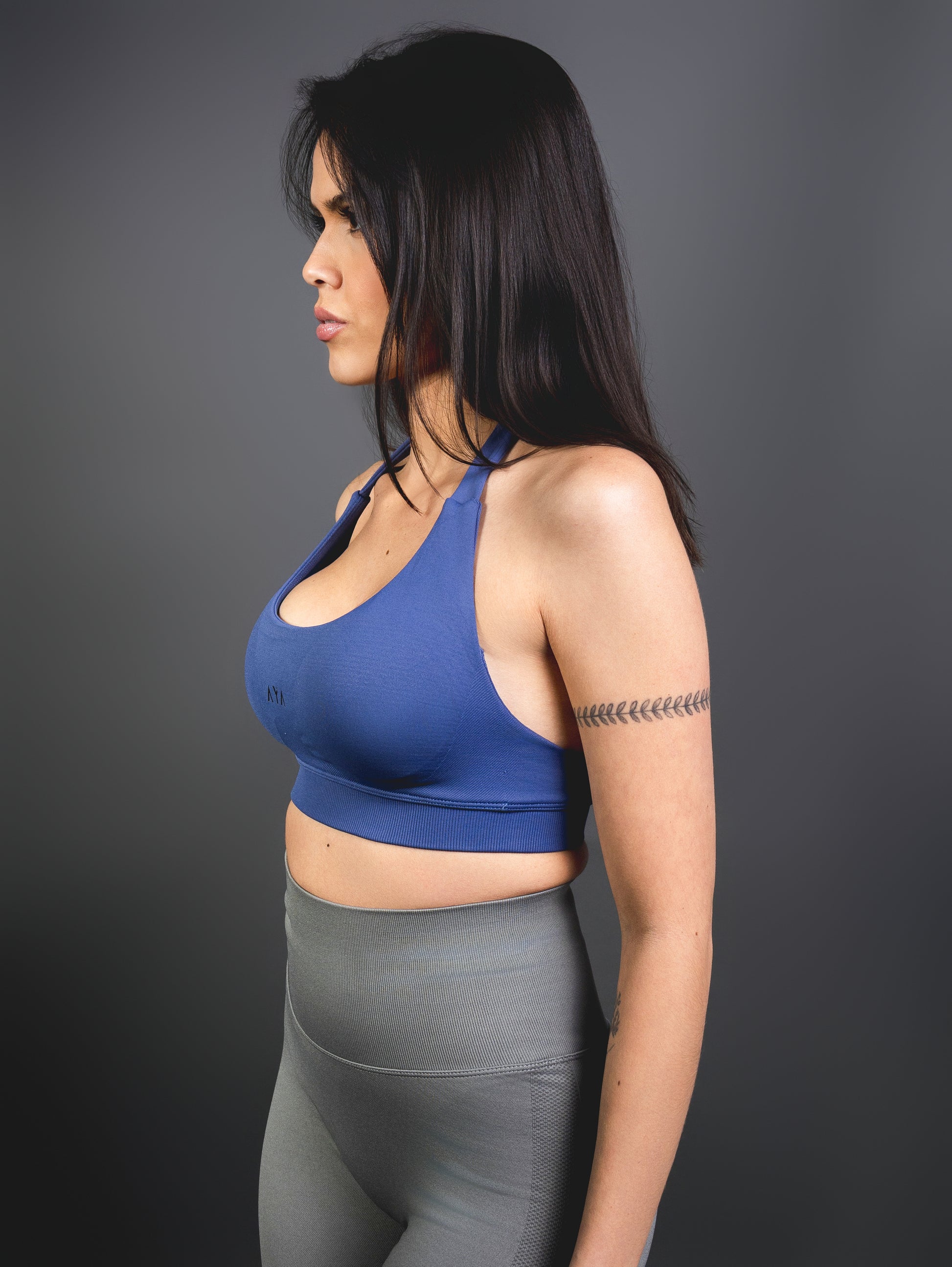 Side view of woman wearing royal blue AYA sports bra and grey seamless leggings – sleek, supportive activewear highlighting a sculpted and confident silhouette.