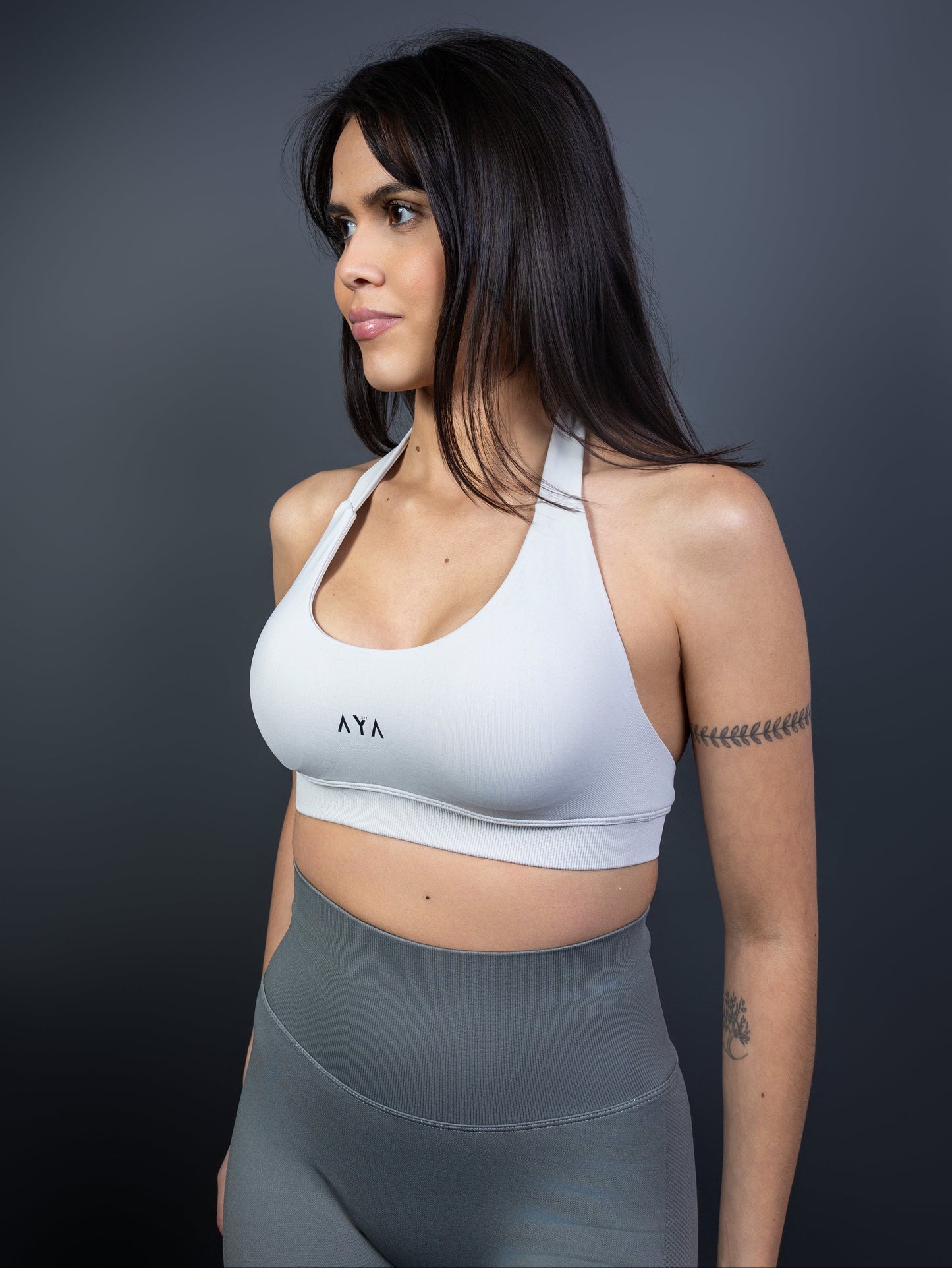 Close-up of woman wearing white AYA halter sports bra and grey seamless leggings – minimalist, sculpting activewear that blends elegance, strength, and feminine energy.