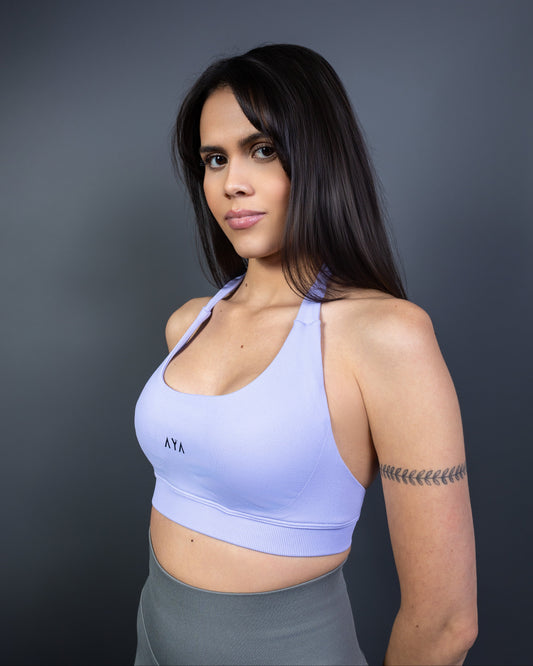 Side view of woman wearing lilac AYA halter sports bra and grey seamless leggings – soft pastel activewear that blends elegance, comfort, and modern femininity.