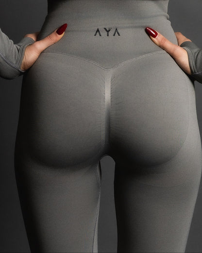 Woman wearing grey high-waisted seamless AYA leggings and black sports bra – sleek, body-hugging fit designed to enhance natural curves and exude quiet confidence.