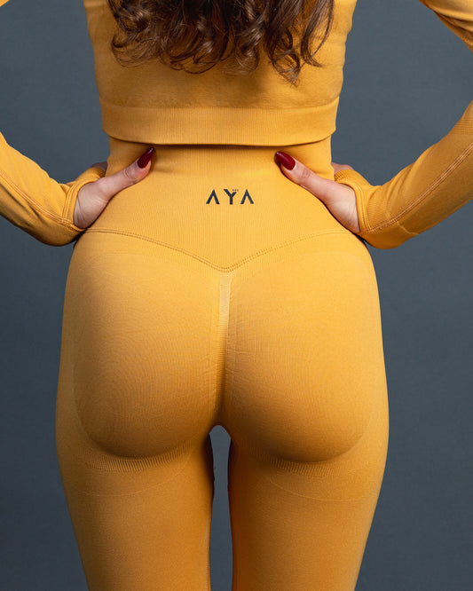 Woman wearing yellow high-waisted seamless AYA leggings and black sports bra – sleek, body-hugging fit designed to enhance natural curves and exude quiet confidence.