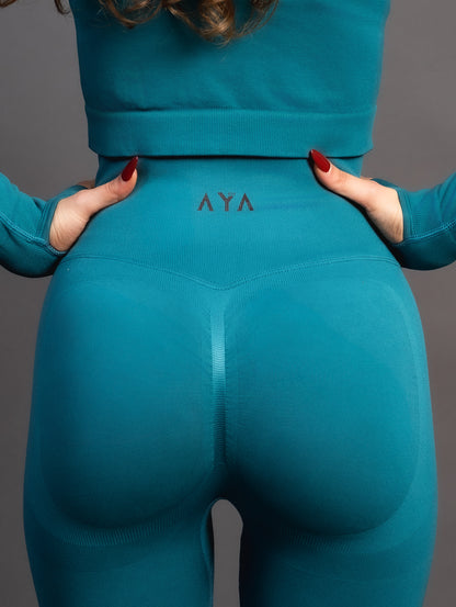 Woman wearing teal high-waisted seamless leggings and black sports bra – sculpting, stretchy gym leggings designed to accentuate curves and provide maximum comfort during workouts