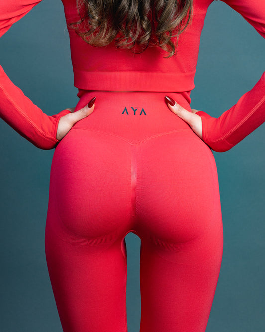 Woman wearing red high-waisted seamless AYA leggings and black sports bra – sleek, body-hugging fit designed to enhance natural curves and exude quiet confidence.
