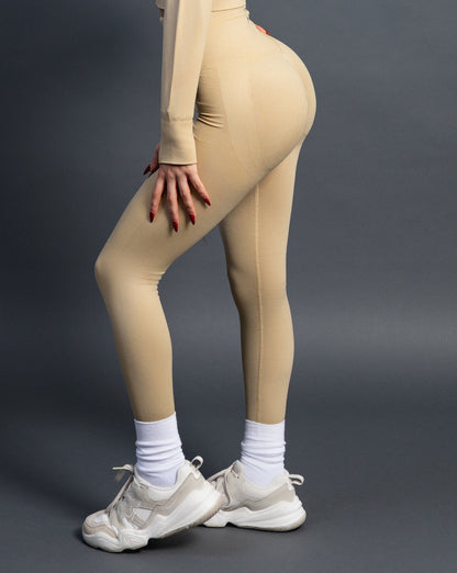 Woman wearing beige high-waisted seamless AYA leggings and white halter sports bra – figure-hugging, sculpting activewear designed for strength and elegance.